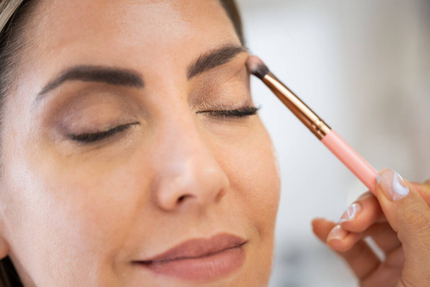 Close-up van een make-up kunstenaar die oogschaduw op haar cliënt aanbrengt. - Foto, afbeelding
