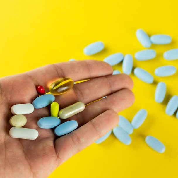 Multi-gekleurde tabletten en capsules op een hand en blauwe tabletten op een gele achtergrond - Foto, afbeelding