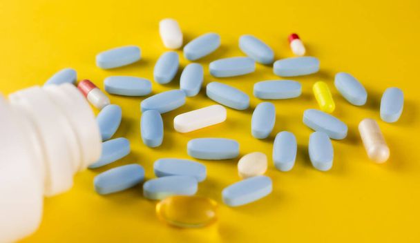 Bouteille de pilule blanche et pilules sur fond jaune, bouteille de pilule blanche, bouteille de pilule bleue avec capsules colorées sur fond jaune - Photo, image