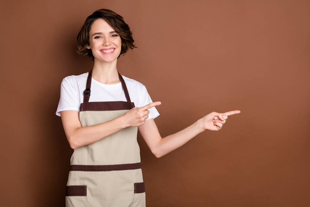 Photo of happy cheerful beautiful lovely woman barista point finger copyspace advertise isolated on brown color background - Foto, imagen