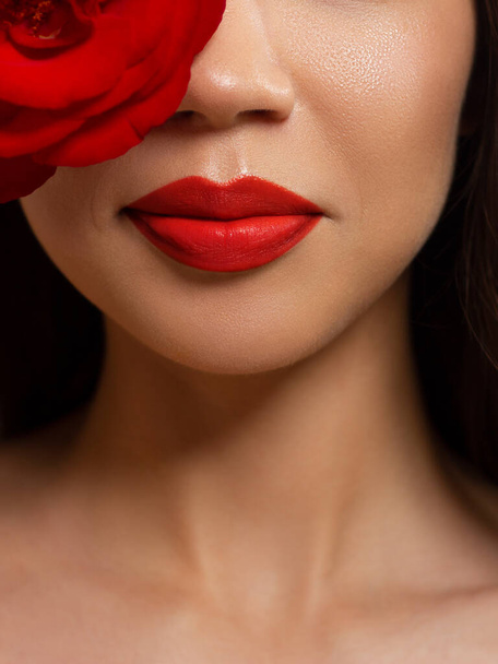 Half a beauty portrait with beautiful fashionable evening make-up with flowers, black jiggles on eyes and extremely long eyelashes. Red lipstick on the lips. Cosmetology and spa facial skin care - Foto, imagen