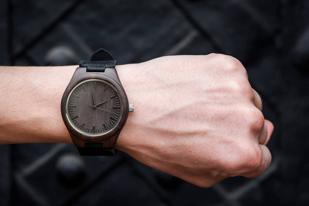 Brązowy drewniany zegarek na rękę ze skórzanym paskiem na męskim nadgarstku na czarnym tle. Zbliżenie. Miejsce na SMS-a. Wysokiej jakości zdjęcie - Zdjęcie, obraz