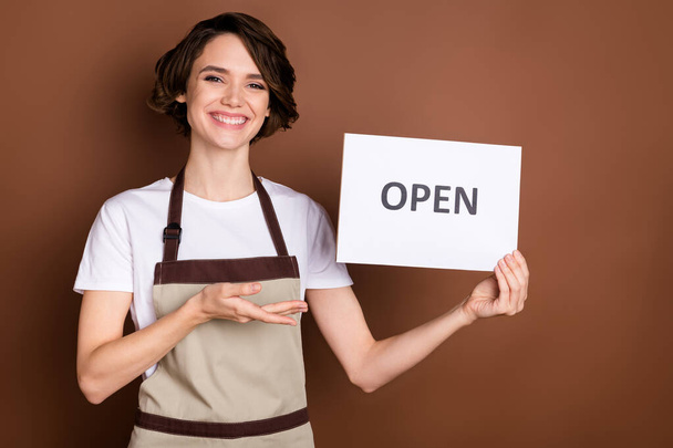 Portrait of lovely cheerful girl shop store seller demonstrating open card promo isolated over brown color background - Photo, image