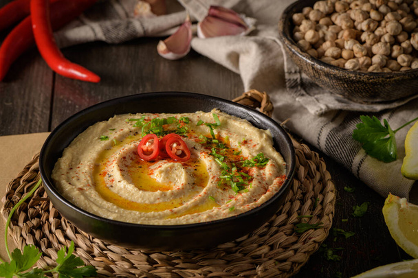 Delicious hummus in ceramic bowl. Colorful snack composition on a black wooden background. - Foto, afbeelding
