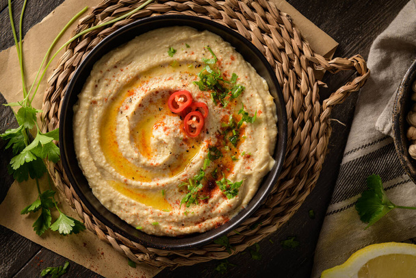 Delicious hummus in ceramic bowl. Colorful snack composition on a black wooden background. - Foto, Imagem