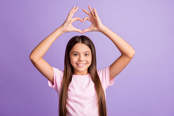 Photo of young schoolgirl happy smile make finger heart figure valentine day cupid isolated over purple color background - Foto, Imagen