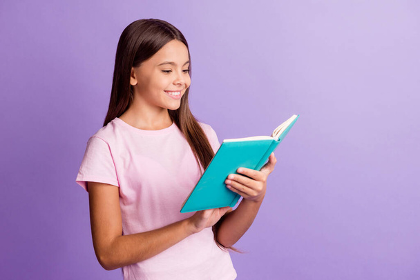 Photo of charming shiny young girl wear pink t-shirt smiling reading book isolated violet color background - Photo, Image