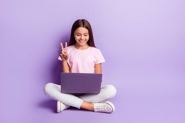 Photo of funny pretty schoolgirl dressed pink t-shirt showing v-sign looking modern device isolated purple color background - 写真・画像