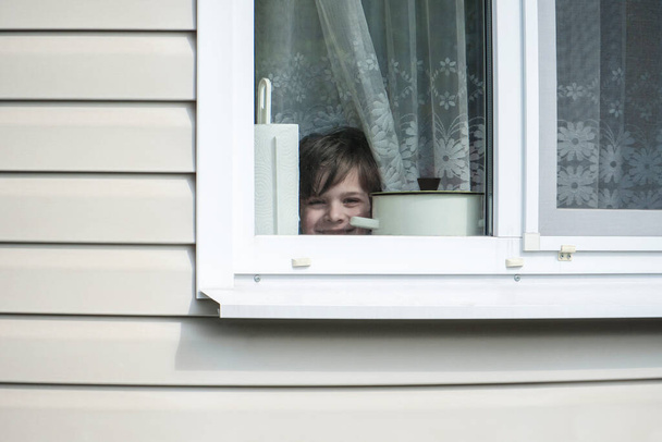Portrét veselého a veselého chlapce dívajícího se oknem do kamery. - Fotografie, Obrázek