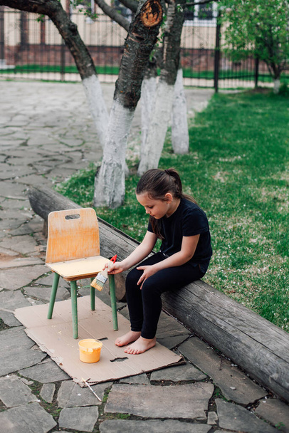 the concept of reusing old things, a child repaints an old chair with yellow paint - Foto, Imagem