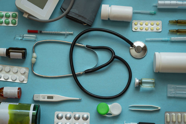 Üst görünüm medikal düzlem: stetoskop, termometre, şırınga, haplar, sprey, mavi arka planda lensler - üst görünüm düz model - Fotoğraf, Görsel