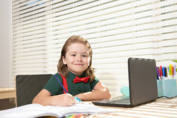 Smart smiling school pupil kid virtual distance learning online, watching remote digital class lesson, looking at laptop computer studying at home, writing notes. - Фото, изображение