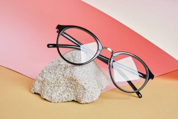 occhiali da vista su un podio di cemento su uno sfondo rosa e beige, composizione di tendenza, occhiali da vista neri alla moda, spazio copia - Foto, immagini