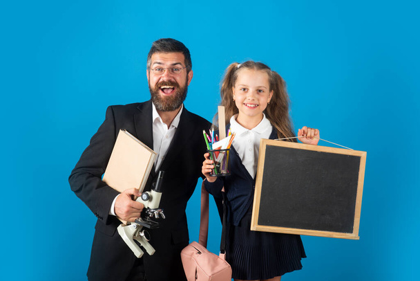 Portrait of smiling teacher and happy pupil schoolgirl ready to school. Portrait of dad and little girls with school supplies, isolated on blue background. - Foto, Imagem