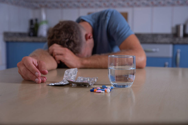 Um homem overdose depois de consumir muitas drogas antidepressivas, o homem desmaiou perto de pílulas médicas. Suicídio por overdose. Close-up sobre o vidro de água e pílulas, fundo embaçado - Foto, Imagem