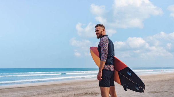 European guy with surfboard on the beach. Looks to the distance - Zdjęcie, obraz
