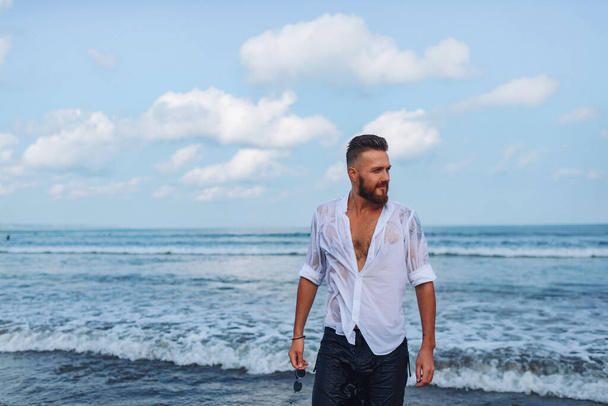 Elegante europeo chico en una camisa blanca sale del mar - Foto, imagen