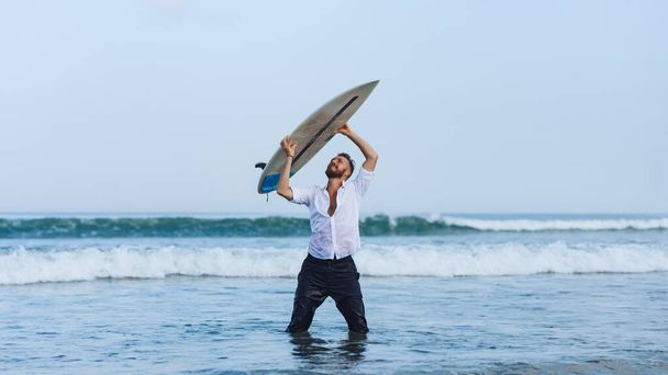 Joven europeo sosteniendo una tabla de surf sobre su cabeza en el mar. - Foto, imagen