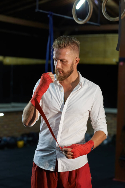 A stylish guy in a shirt is boxing. A man tired after work winds bandages on his arm - Photo, Image