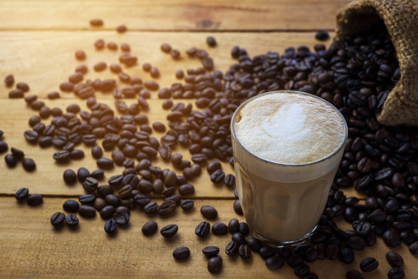 Gorące cappuccino kawy i ziarna kawy na starszym drewnianym stole w godzinach porannych. Przerwa na kawę. - Zdjęcie, obraz