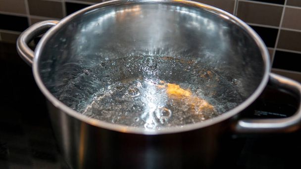 Close up view of hot boiling water in a pot at the kitchen. Water produce bubbles when heated. Selective focused on subject. - Zdjęcie, obraz