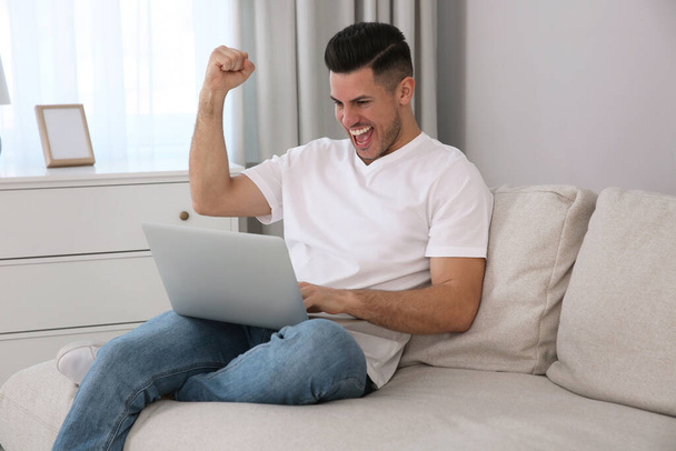 Emotional man participating in online auction using laptop at home - Fotó, kép