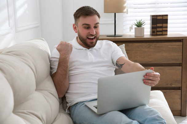 Emotional man participating in online auction using laptop at home - Φωτογραφία, εικόνα