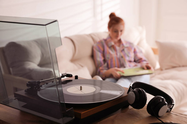 Young woman with vinyl discs in living room, focus on turntable - Fotó, kép