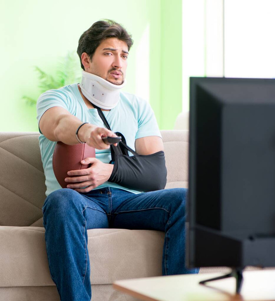 Hombre con lesión en el cuello y el brazo viendo fútbol americano en la televisión - Foto, Imagen