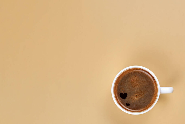 A cup of freshly brewed coffee with hearts inside on a beige background, copy space. - Fotografie, Obrázek