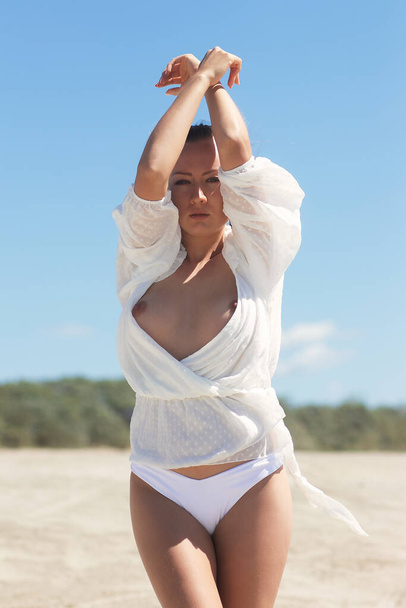 Приваблива чуттєва молода жіноча модель в білій блузці, що розкриває голі груди, що стоять з закритими очима і піднятими руками, насолоджуючись свободою і сонячним світлом на тлі блакитного неба в літній природі
 - Фото, зображення