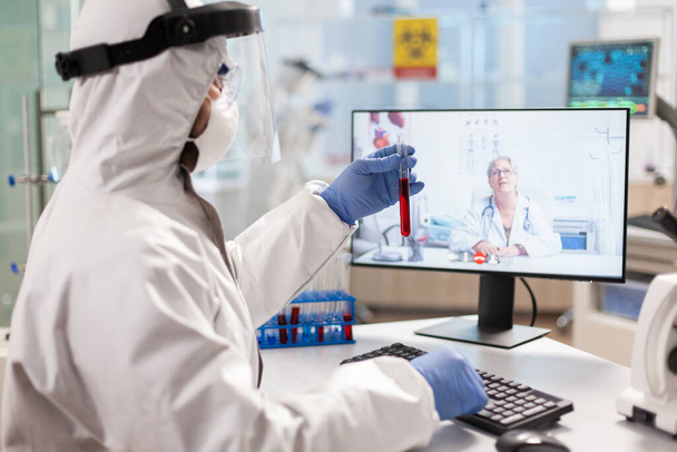 Investigador de laboratorio discutiendo con en videollamada vestido con traje de ppe - Foto, imagen