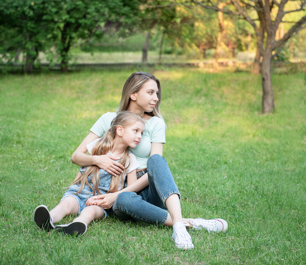 Foto van vrouw en kind die samen op het gras zitten en plezier hebben - Foto, afbeelding
