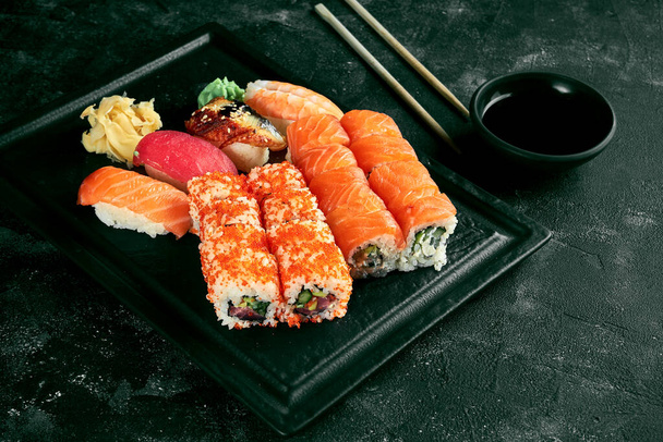An appetizing sushi set consisting of various uramaki with salmon, avocado and tobiko caviar and nigiri. Japanese traditional cuisine. Food delivery. Black background - Φωτογραφία, εικόνα
