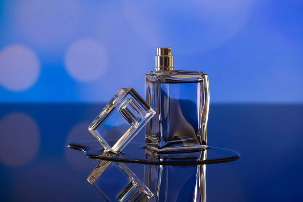 Unbranded perfume bottle on glassy surface, blurred blue background. Beauty and product photography concept - Photo, Image