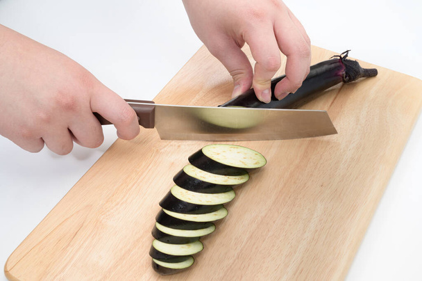 Une main qui coupe l'aubergine sur une planche à découper. - Photo, image