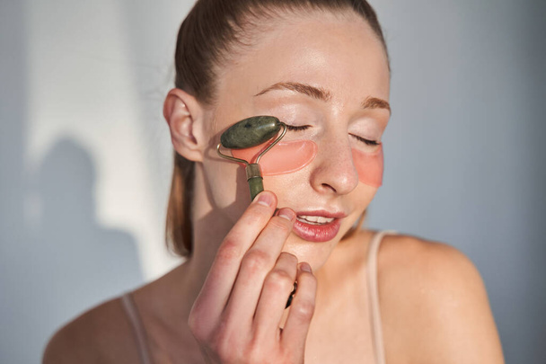 Girl with vitiligo skin applying patches under eyes with massage roller - Fotoğraf, Görsel