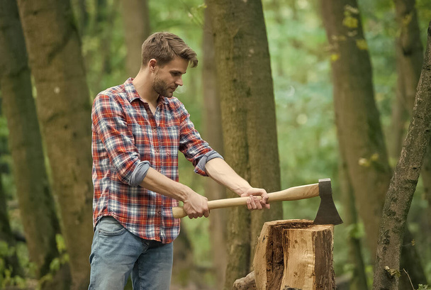 Muscled man in checkered shirt with axe in forest, male activity - Foto, Imagem