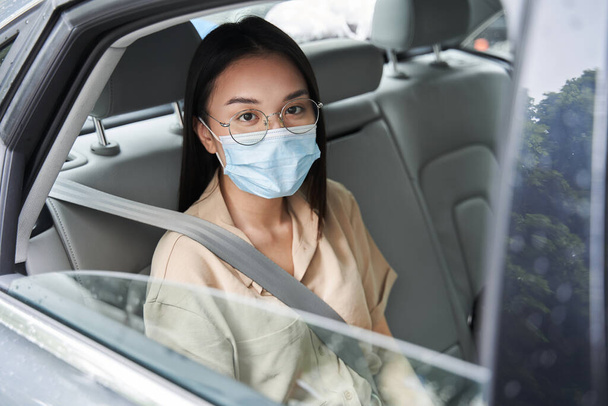 Businesswoman wearing protective mask is sitting on back seat of the car - Fotoğraf, Görsel