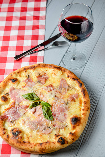 Glass of red wine with pizza on cutting board on rustic wooden table. Italian cuisine concept, pizza with ham and cheese, white background. - 写真・画像