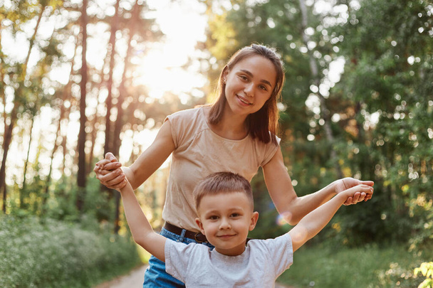 Outdoor portrait of beautiful woman mother posing with her little attractive son, playing and having time in forest or park together, weekend in open air in nature, - Fotografie, Obrázek