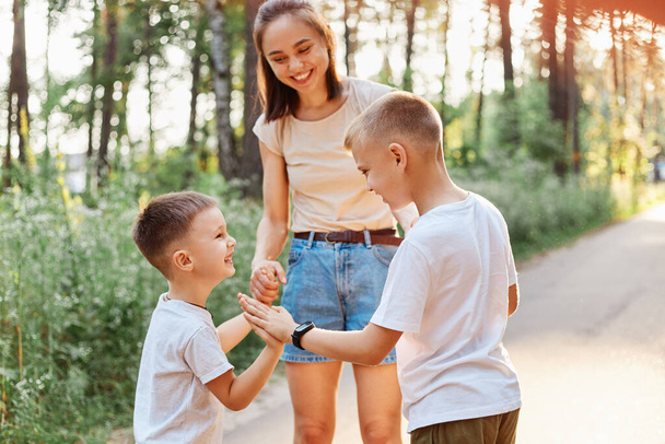 Family having fun while walking in summer park and laughing, little boy gives a high five to his elder brother, happy children standing near their smiling mother. - Foto, immagini