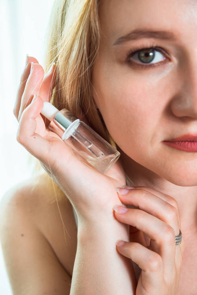 Cosmetical bottle in woman's hand closeup with a part of her blurred face on the right side. Cosmetics and treatment concept. - Photo, Image