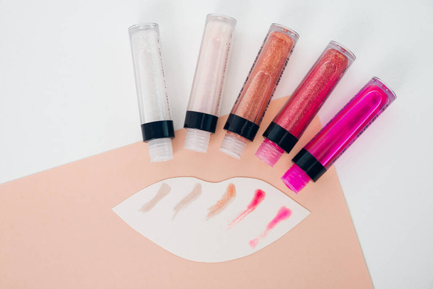 A set of five opened lip glosses and white figure in the shape of lips with lip gloss colores strocks. Lip gloss testers. - Photo, Image