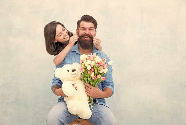 Moustache are classy. Happy daughter twirl fathers mustache. Little child and bearded man hold flowers and toy. Barbershop care. Barber shop. Hair salon. Family barbershop, copy space - Φωτογραφία, εικόνα