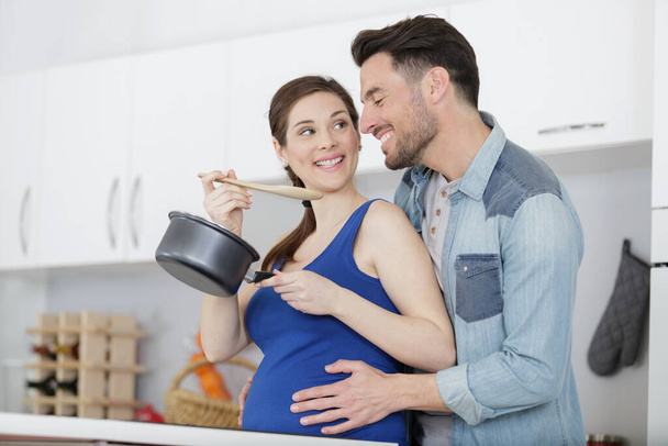 man trying his pregnants wifes sauce in their kitchen - Φωτογραφία, εικόνα