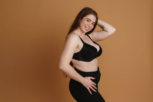 Smiling young plus size woman wearing bra posing over beige wall background - Foto, immagini