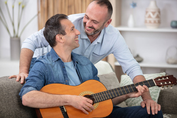 couple with guitar flirting on sofa at home - Foto, Bild