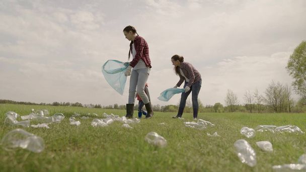 A volunteer team collects garbage in trash bags, a happy family and a small child clean the street from dirty plastic on the ground, preserve a clean environment on a round planet - Фото, изображение