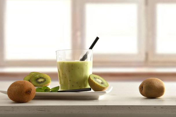 Fruit breakfast with glass of kiwi drink on plate and container cut fruit around on table and window background. Front view. - Foto, Bild